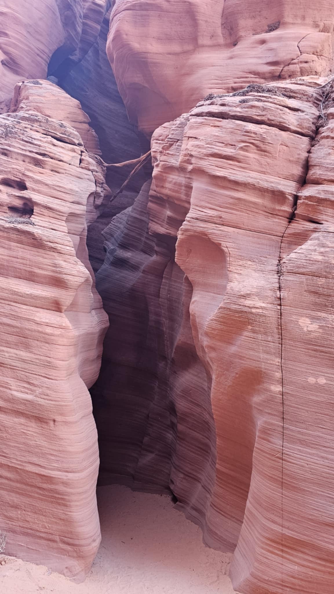 Narrow crack entrance to Canyon X from outside, layered pink sandstone walls