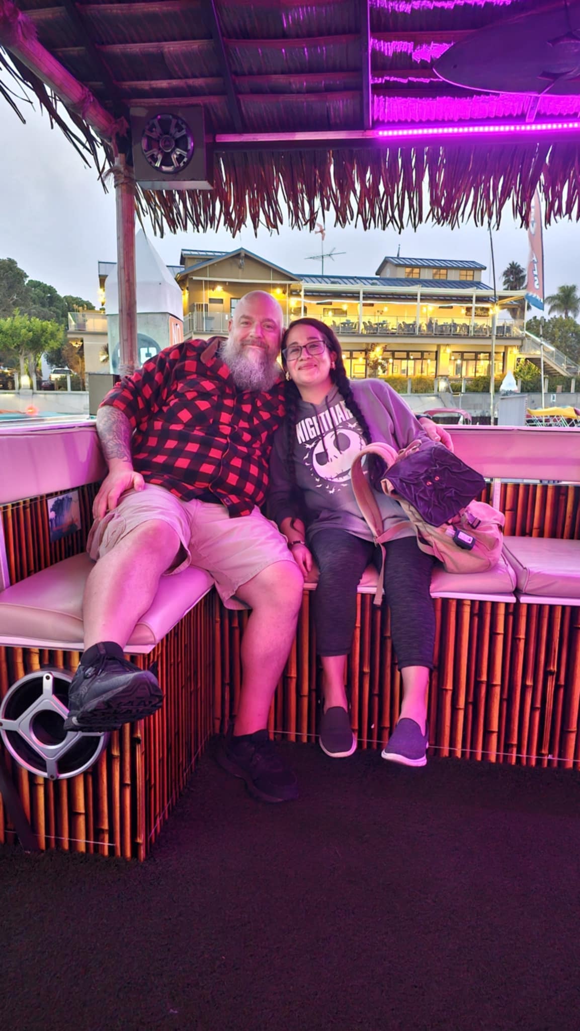 Jason and Delia on the Mission Bay Tiki boat cruise under pink neon lights and a thatched tiki roof