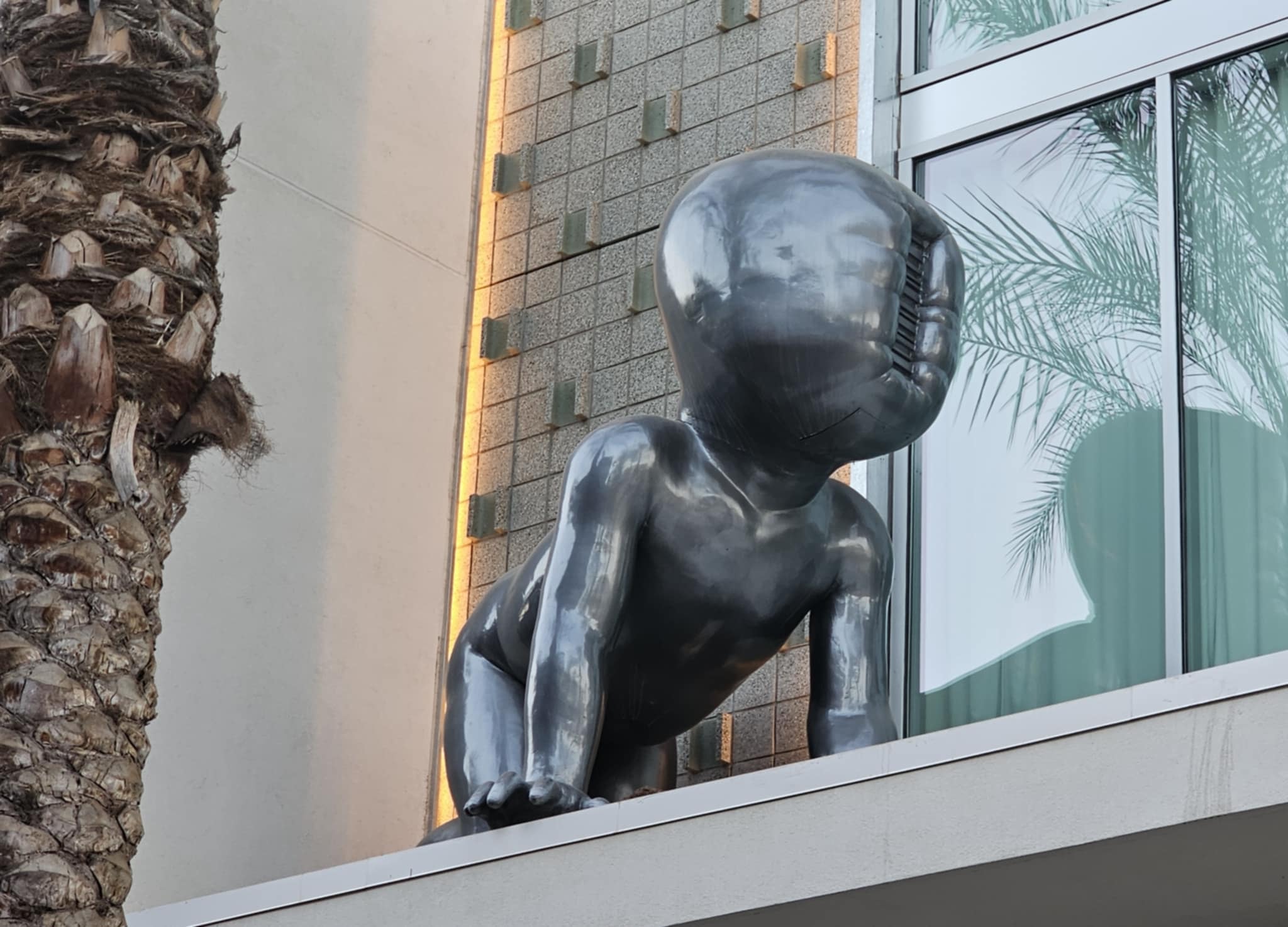 Large black sculptural figure on a Palm Springs building facade with palm trees