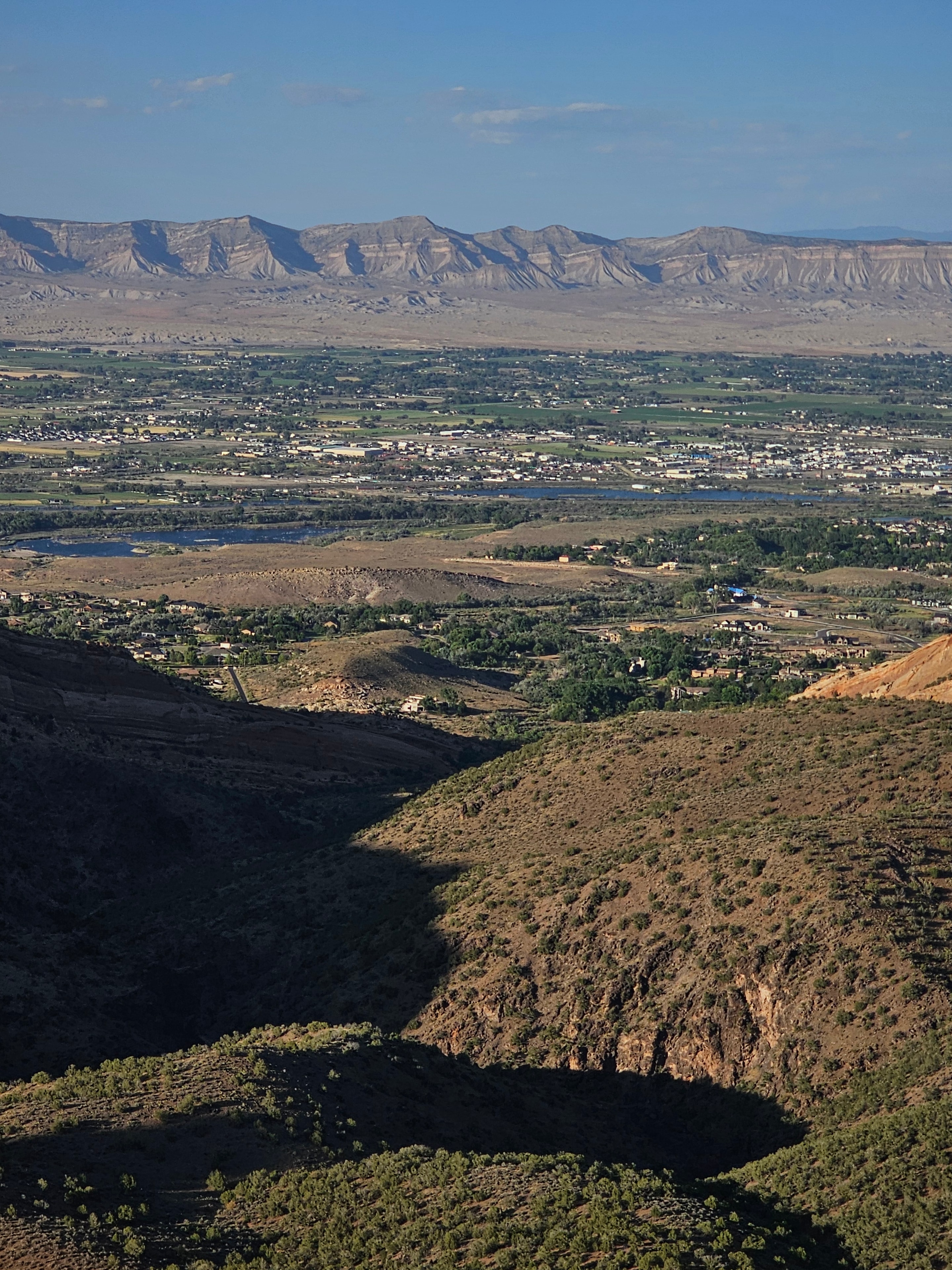 Grand Valley wide panoramic from the canyon rim at Colorado National Monument — Grand Junction, sheer canyon wall foreground, Rocky Mountains in the distance — LOVING LIFE HAVING FUN Brinkley Z3400