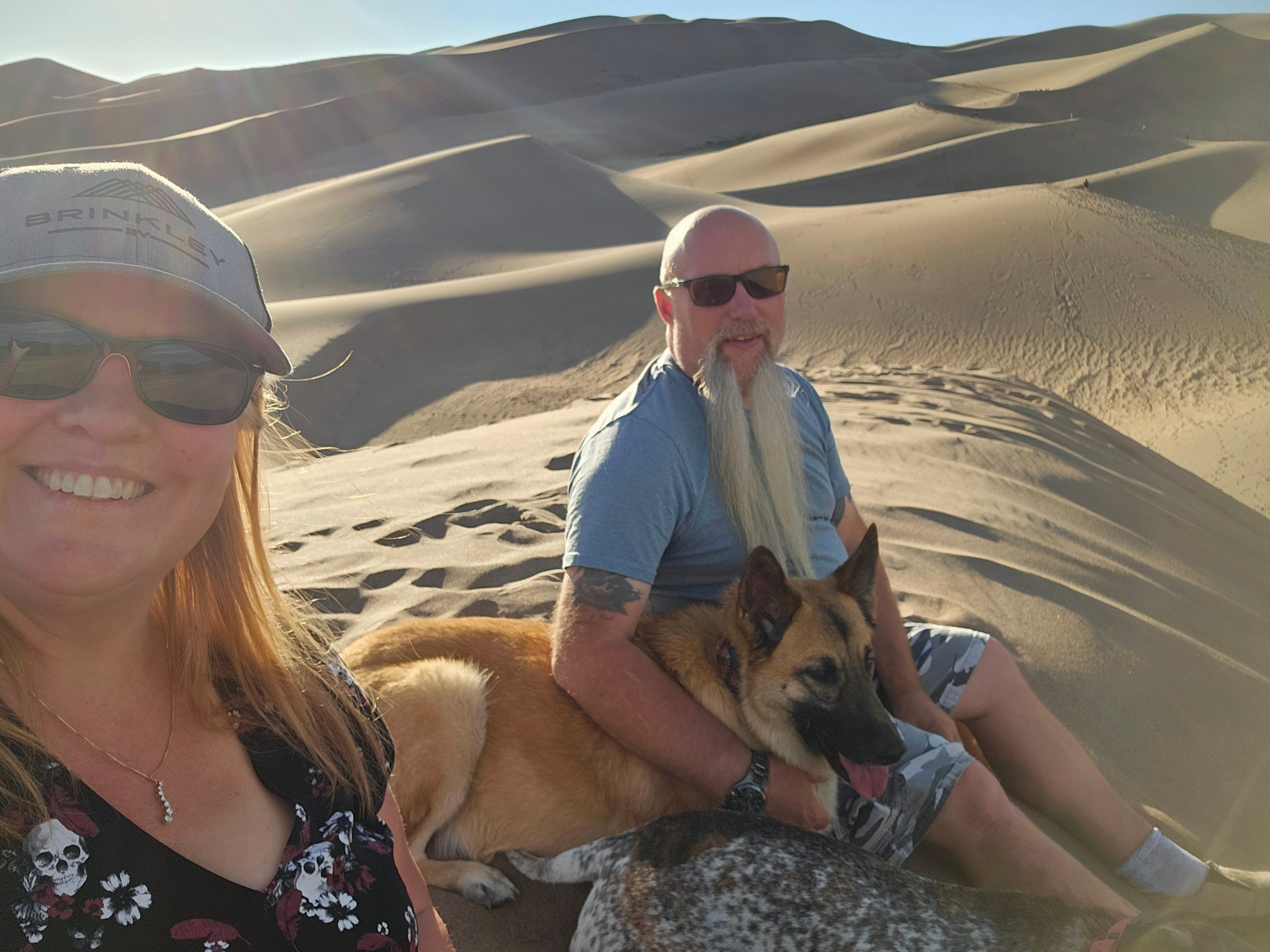 Tina, Joe, and Zero selfie on the Great Sand Dunes — Brinkley cap, massive dune field behind, golden hour light — LOVING LIFE HAVING FUN Brinkley Z3400