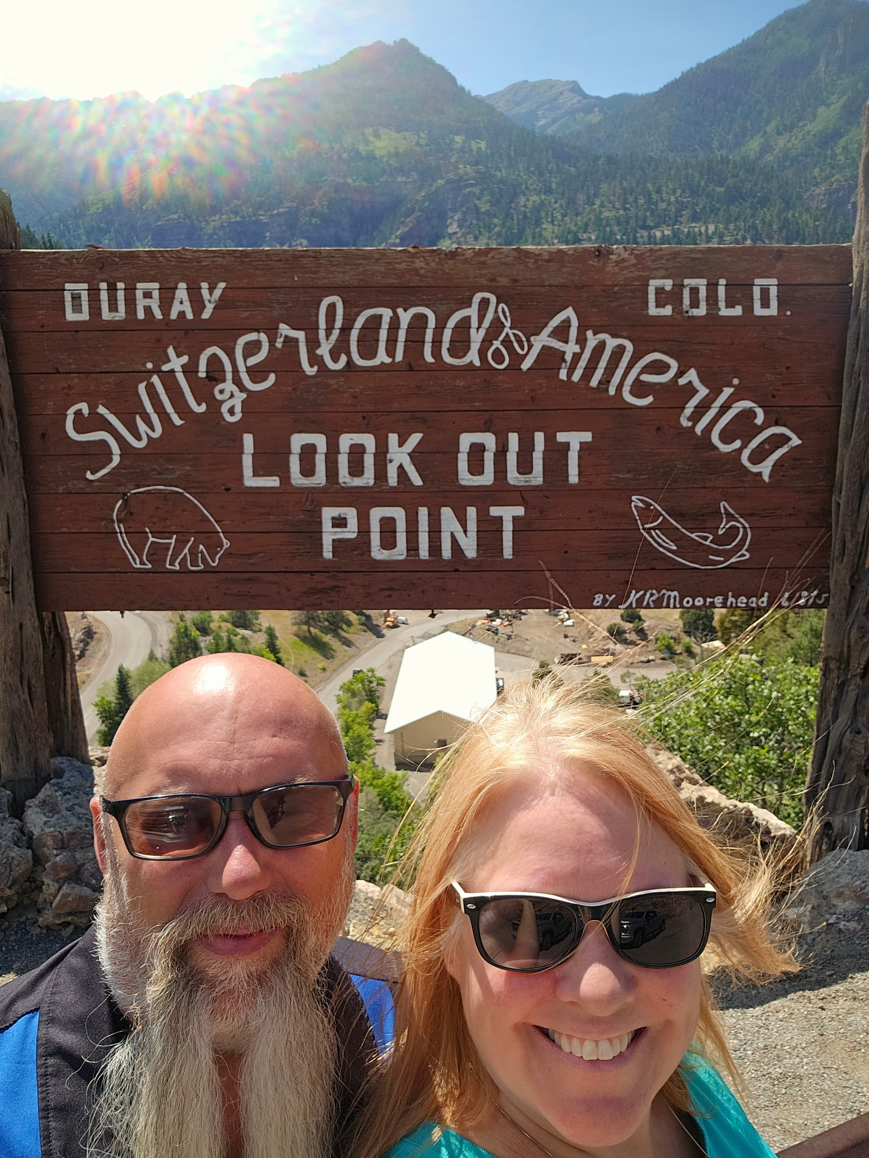Joe and Tina selfie at the Ouray Switzerland of America Look Out Point wooden sign, canyon valley behind — LOVING LIFE HAVING FUN Brinkley Z3400