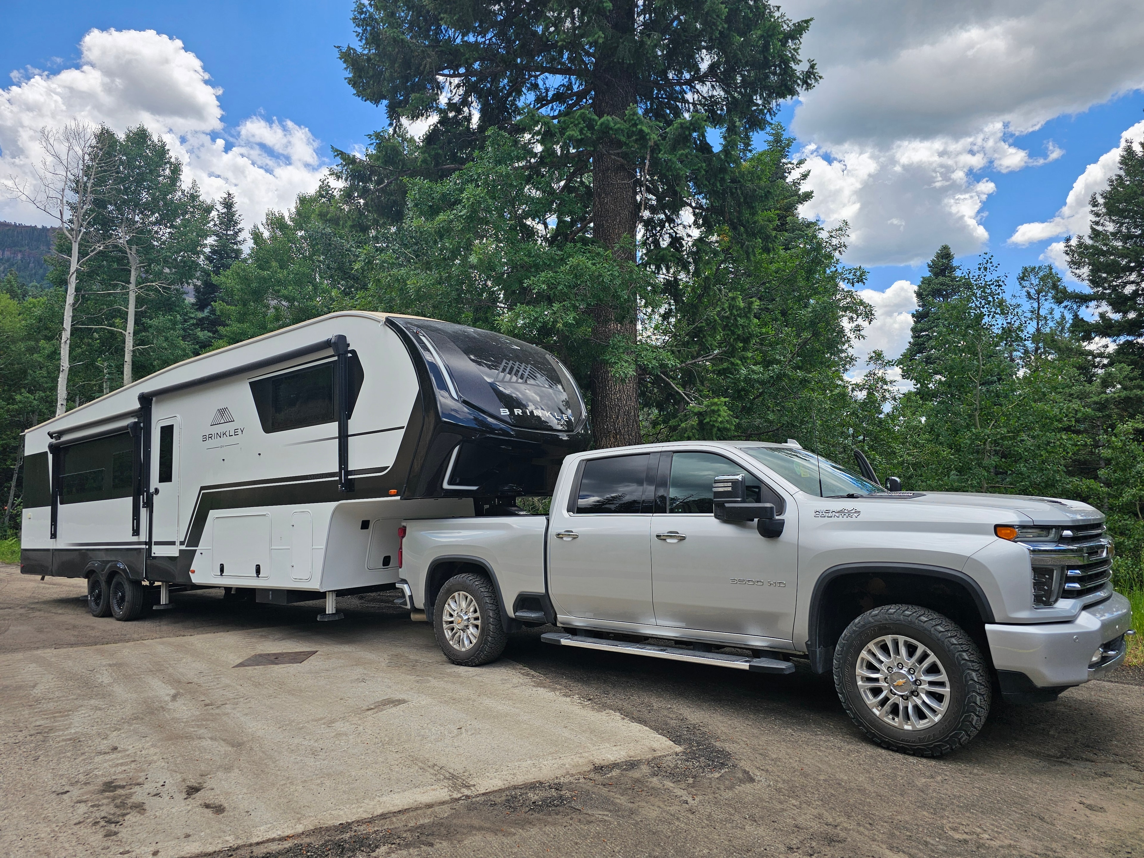 Brinkley Z3400 and truck parked roadside on Wolf Creek Pass — spruce and aspen forest, blue sky and clouds, South Fork, Colorado — LOVING LIFE HAVING FUN