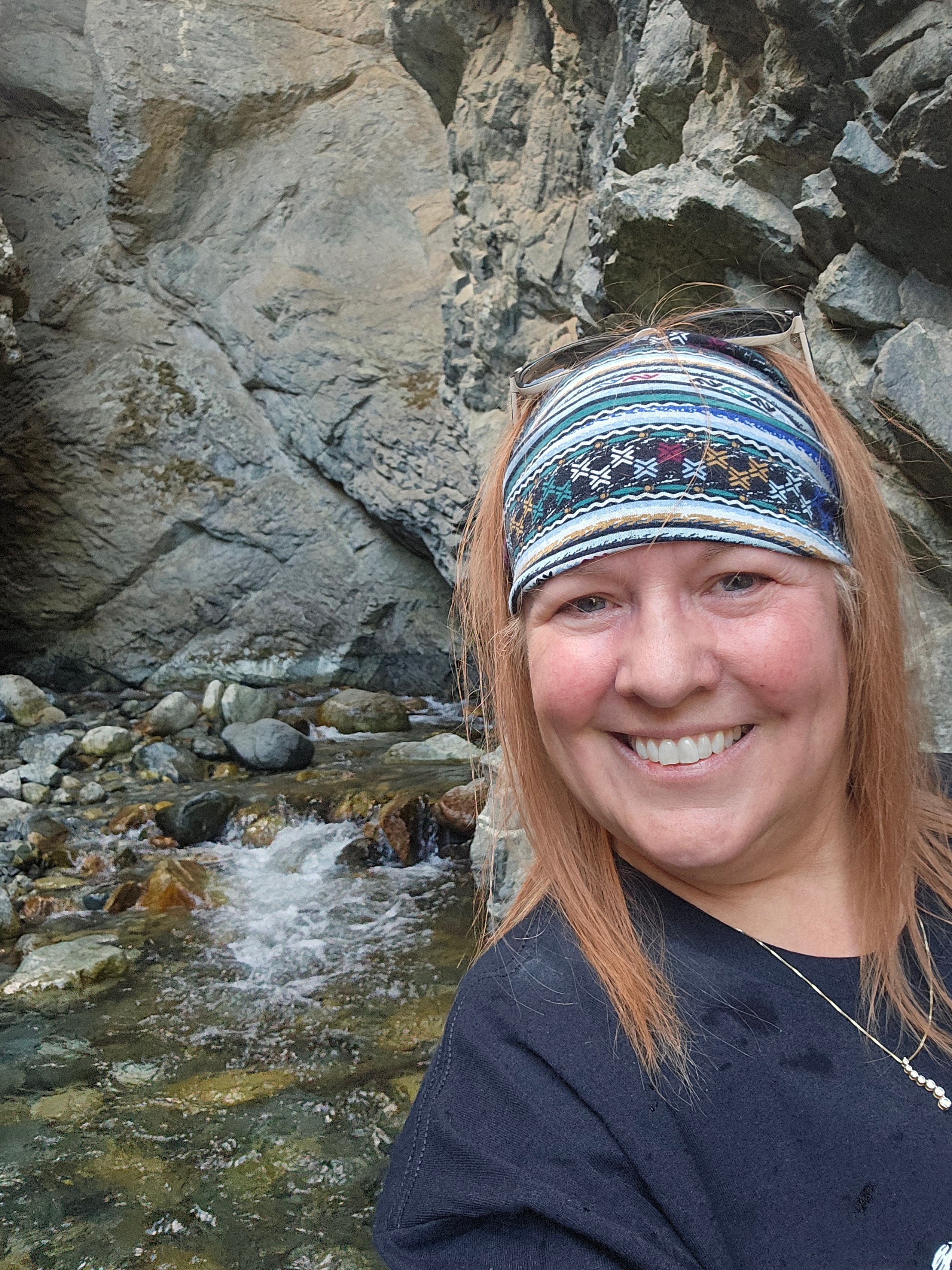 Tina smiling inside the Zapata Falls cave — rocky cave walls, ice and water behind her, Alamosa, Colorado — LOVING LIFE HAVING FUN Brinkley Z3400