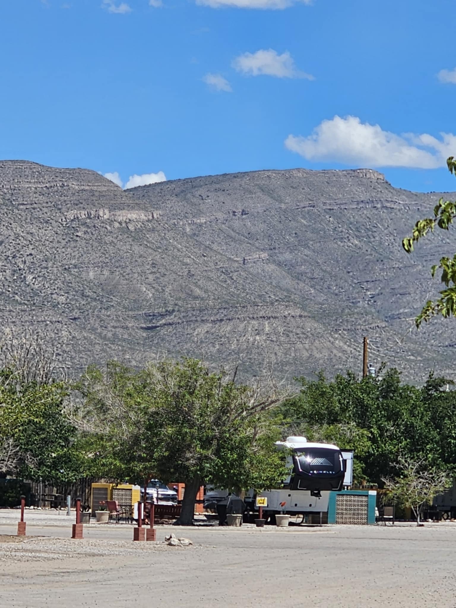 Brinkley Z3400 parked at the KOA campsite in Alamogordo — the fifth wheel visible through the trees with the dramatic layered Sacramento Mountains filling the background under a blue sky