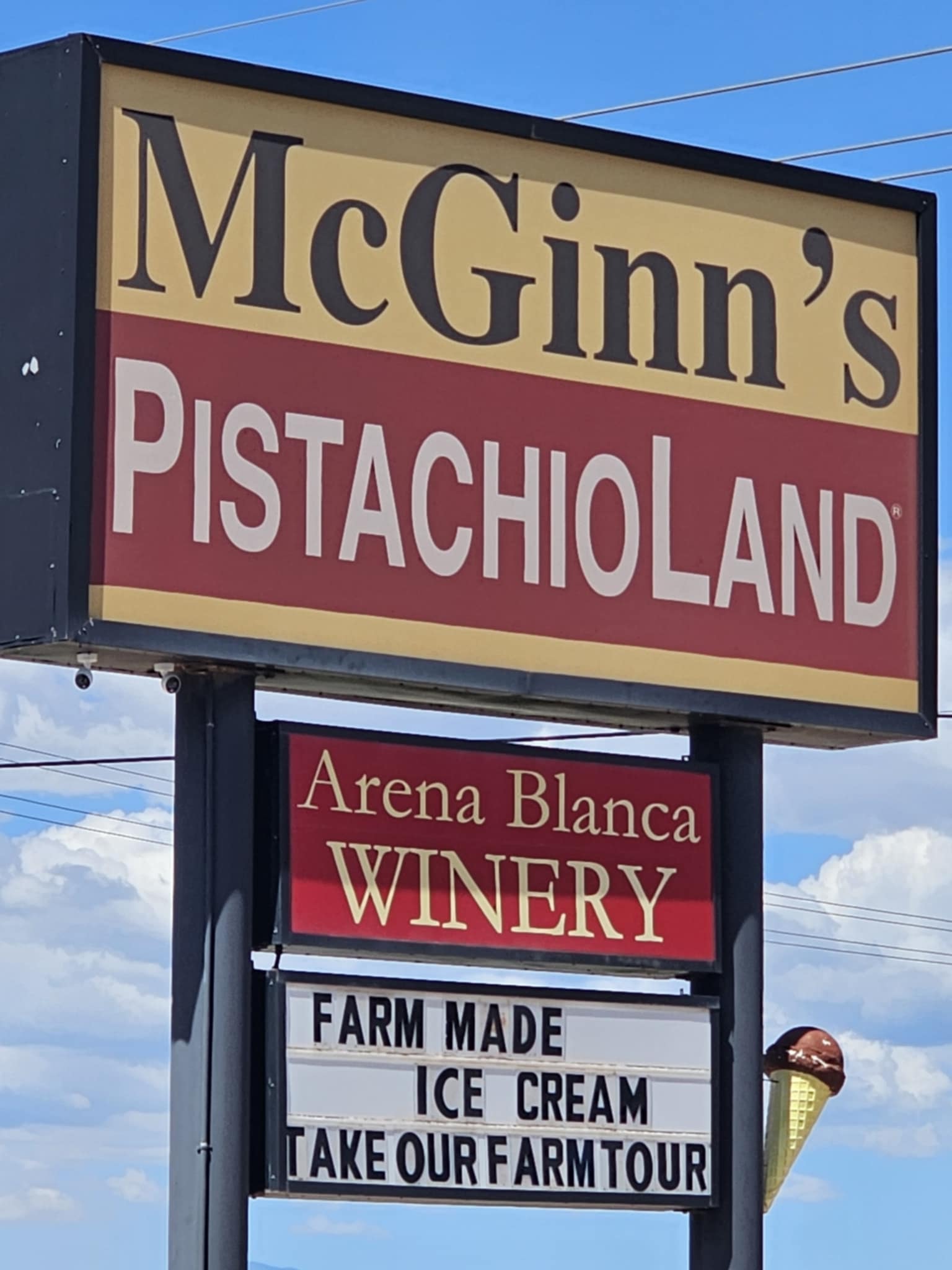 McGinn's PistachioLand sign — close-up of the large roadside sign with Arena Blanca Winery below and a marquee reading Farm Made Ice Cream Take Our Farm Tour, blue sky behind