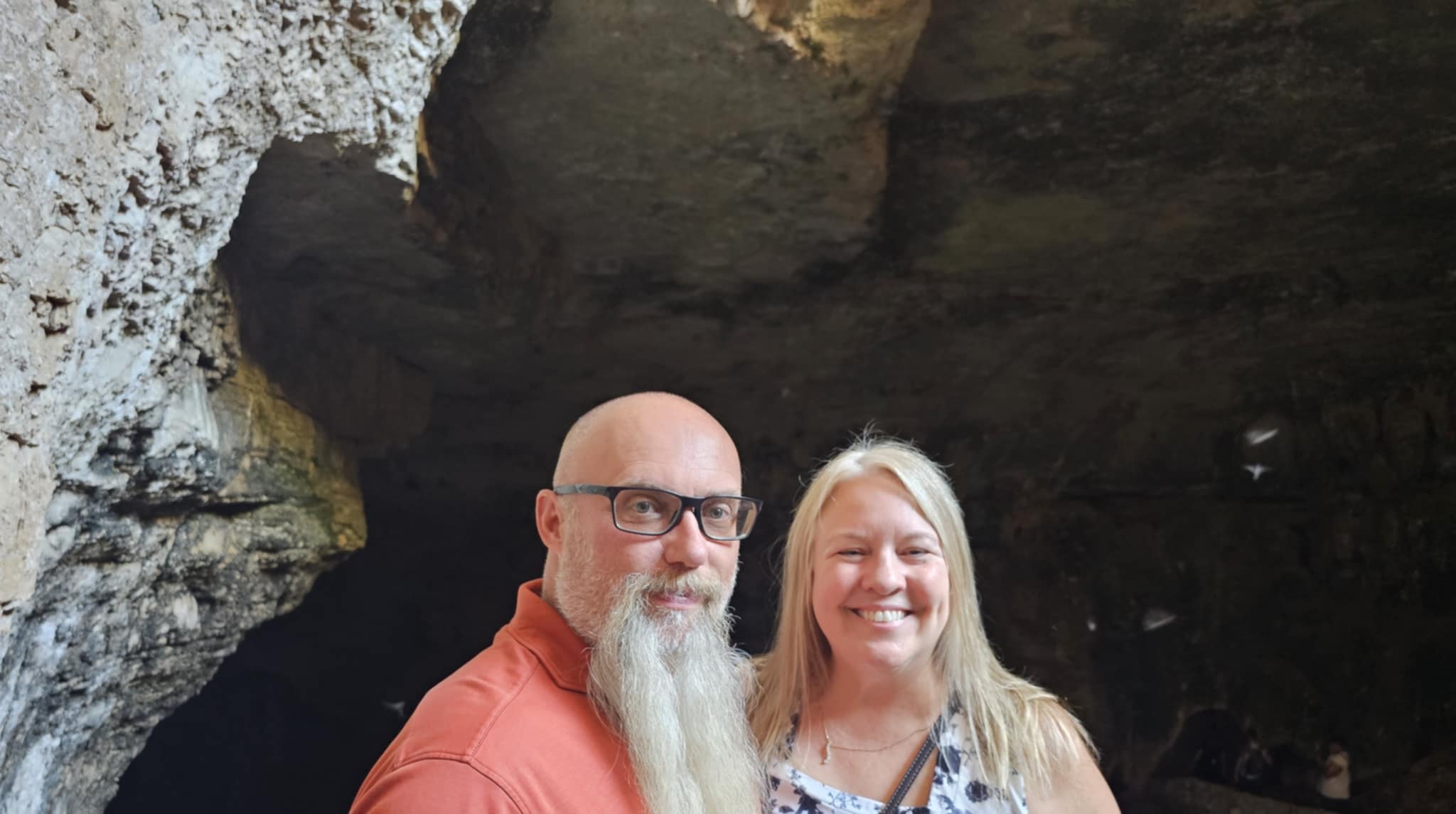 Joe and Tina at the natural entrance of Carlsbad Caverns — the rough limestone cave walls and dark cave passage opening behind them