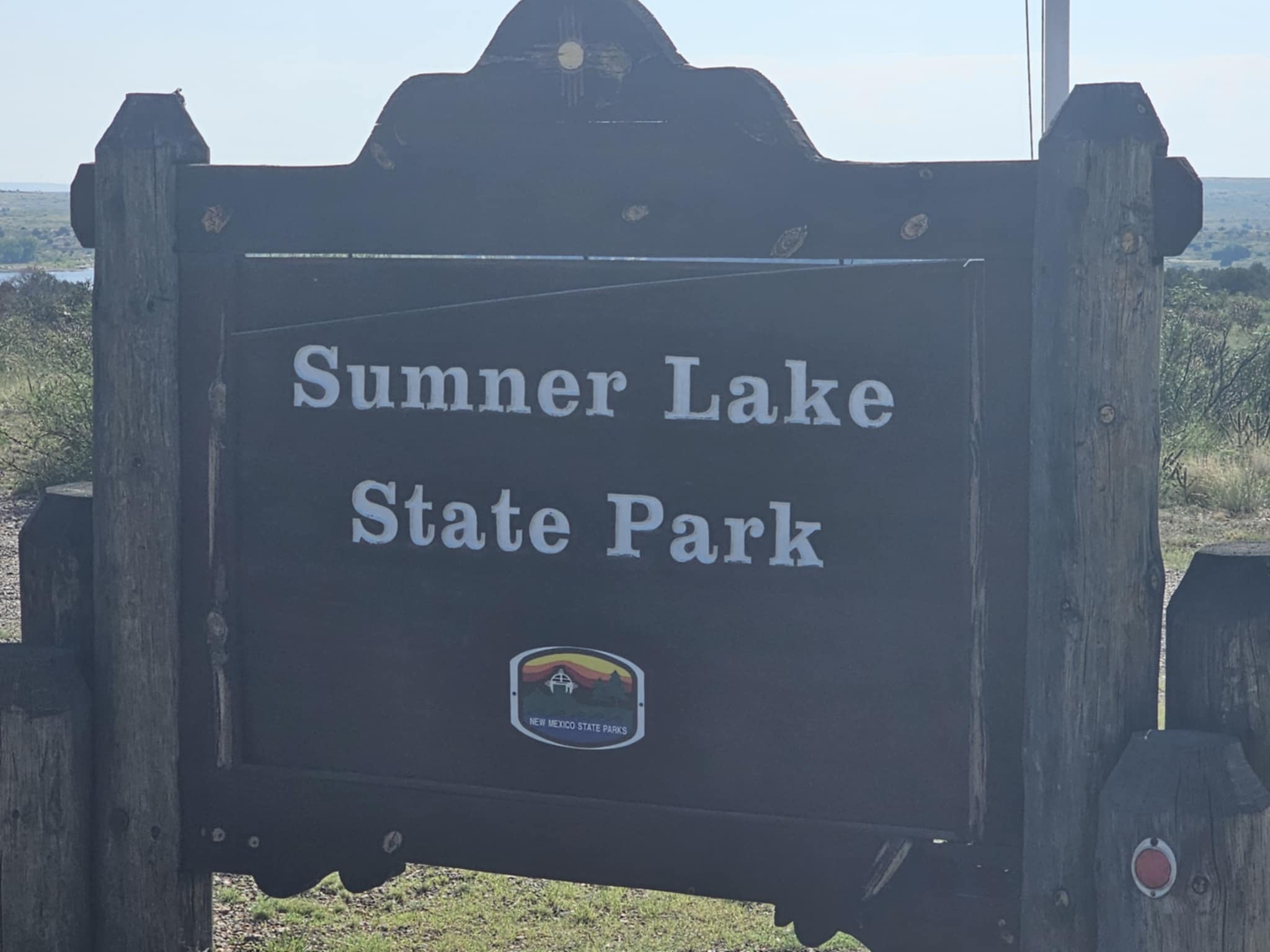Wooden entrance sign for Sumner Lake State Park near Fort Sumner, New Mexico, with the New Mexico State Parks badge and the Pecos River valley visible in the background