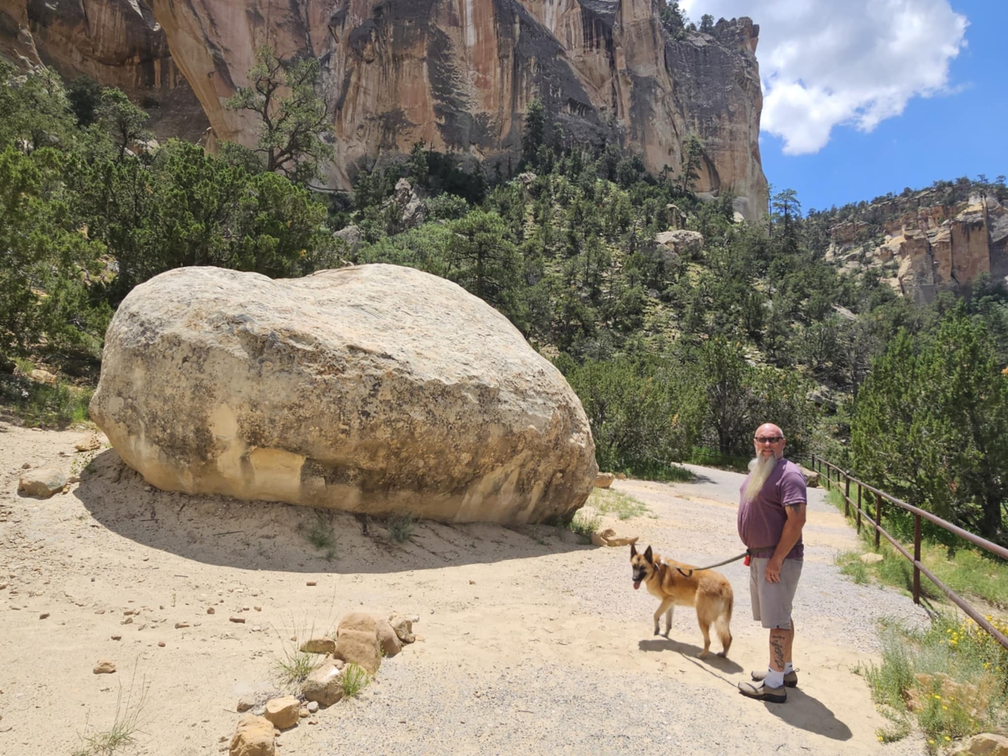 Joe and Zero on the La Ventana trail beside a massive fallen sandstone boulder with the towering arch cliffs and green canyon walls rising behind them