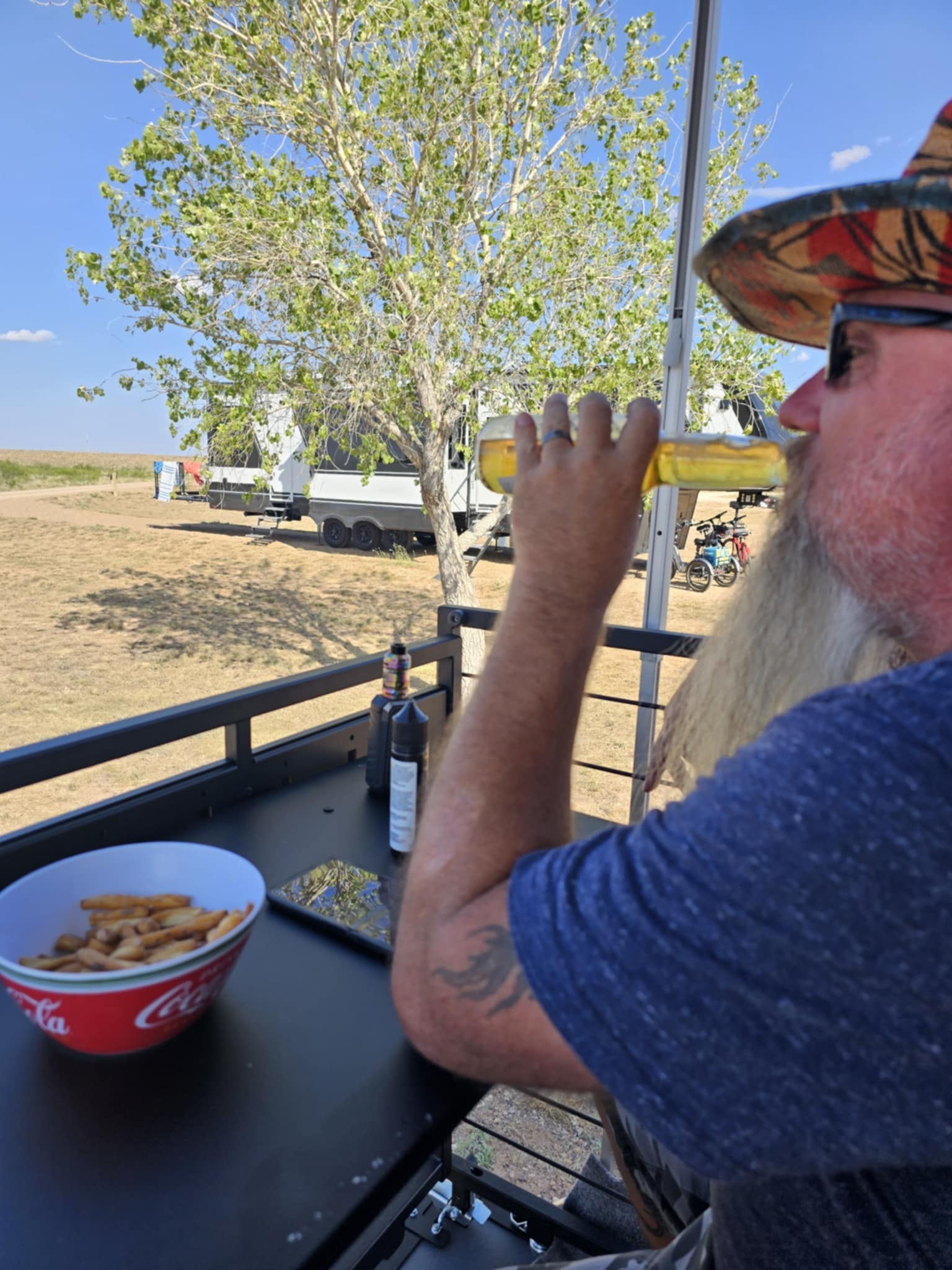 Joe relaxing on the Brinkley patio at Ute Lake State Park, enjoying a cold beer with a bowl of snacks on the outdoor kitchen counter and the campground stretching out behind him