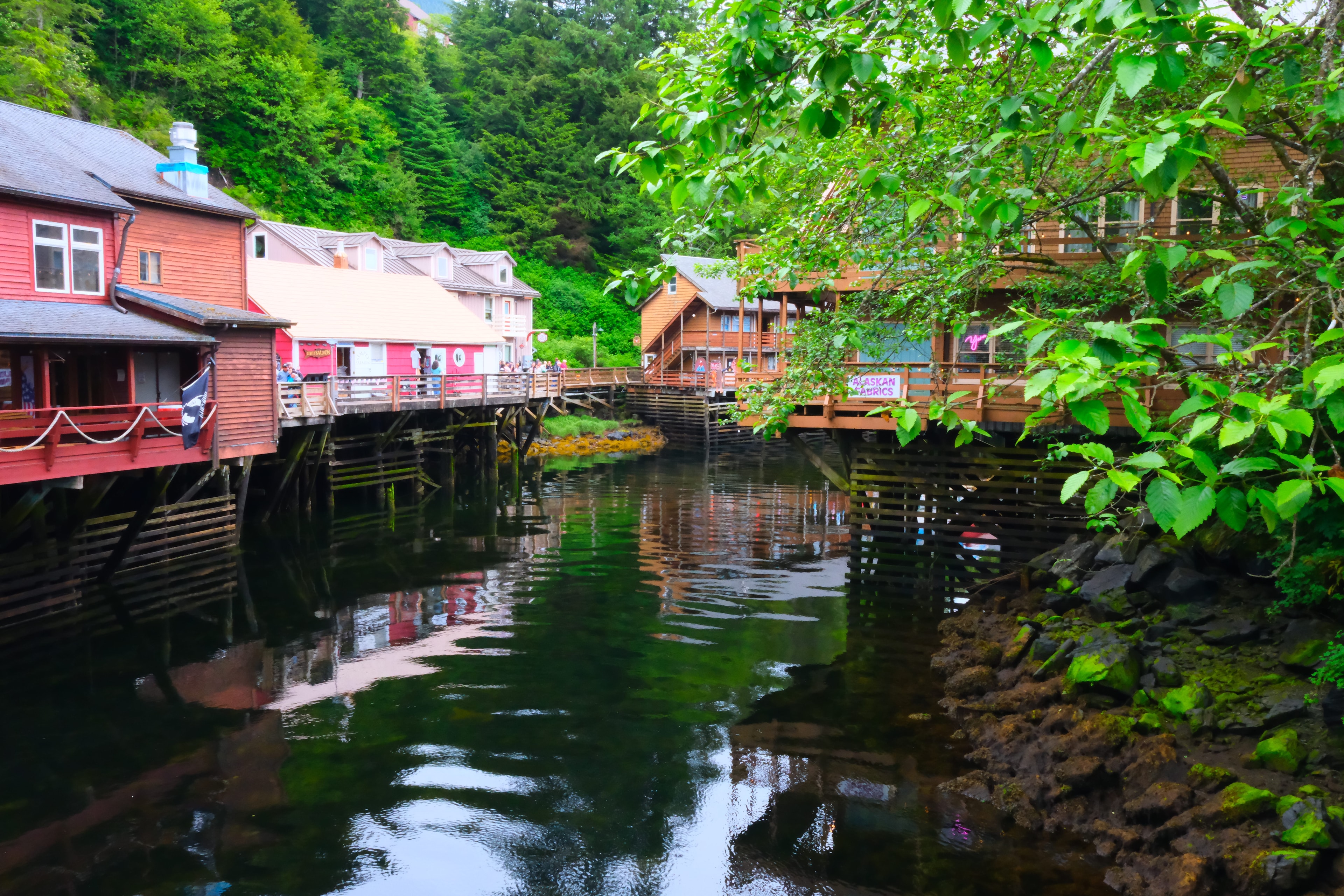 Creek Street boardwalk wide shot — colorful historic buildings on stilts reflected in Ketchikan Creek below