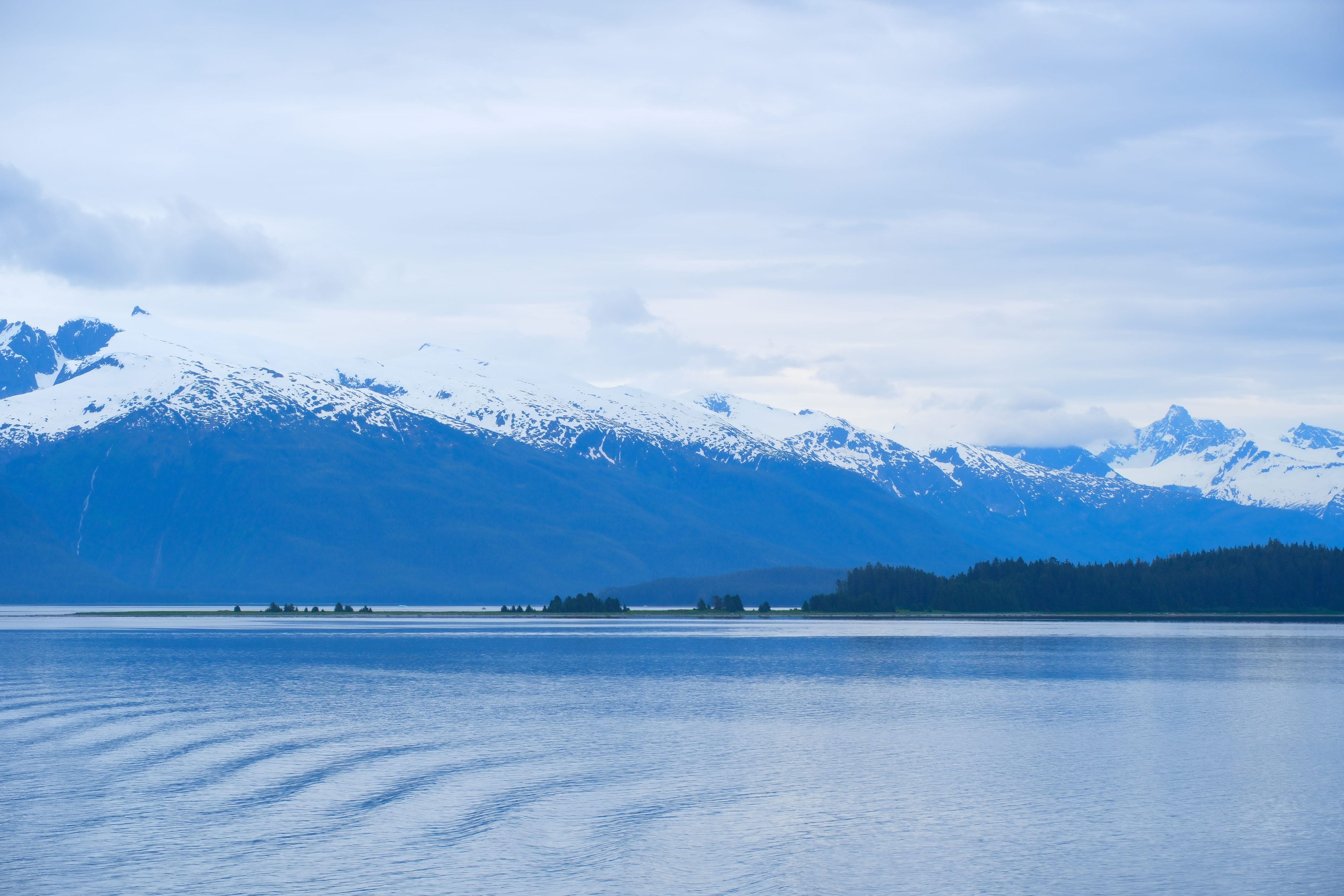 Wide water view with forested island and layered snow-capped mountains