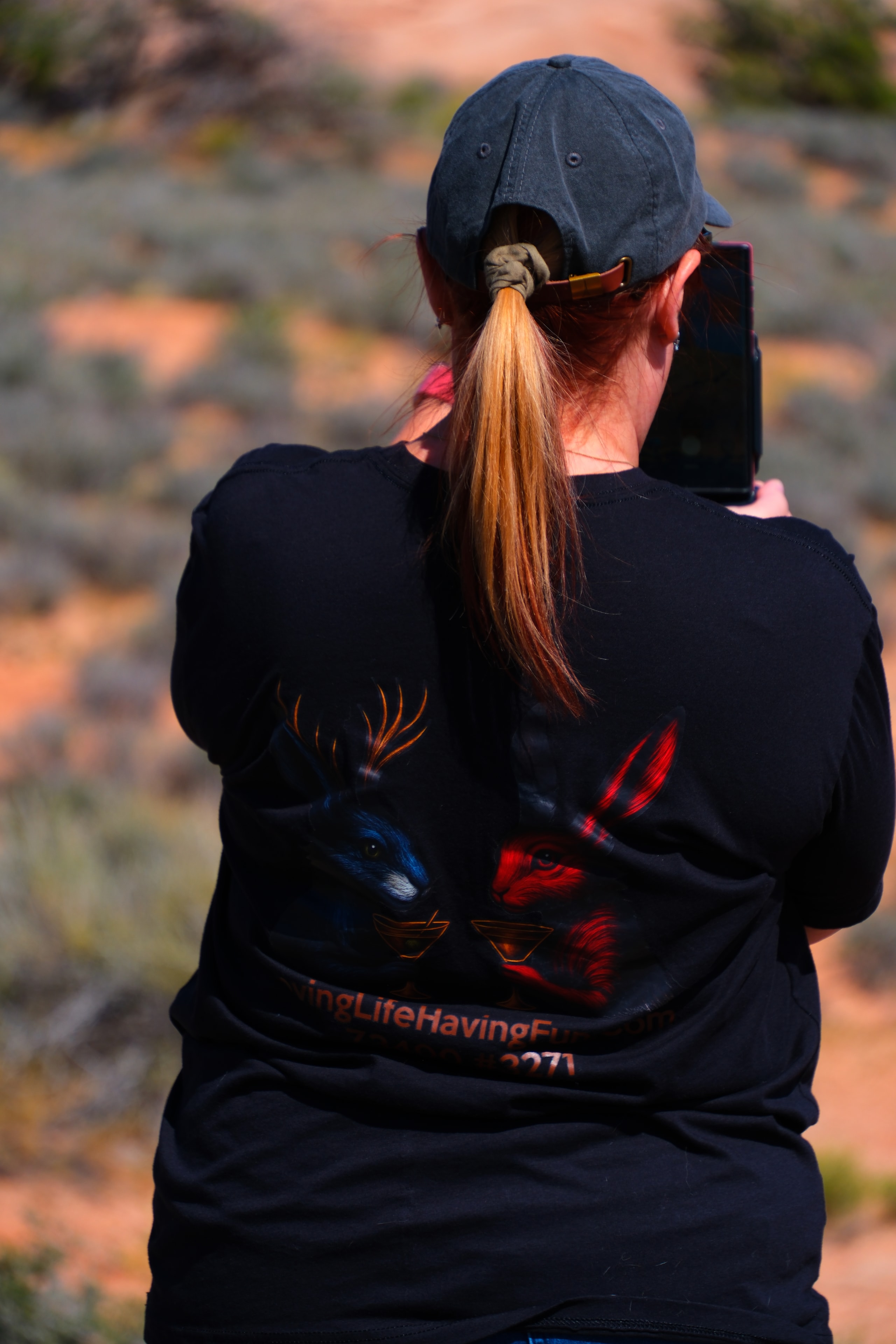 Tina shooting photos with camera wearing LLHF shirt with red rock formations behind at Arches National Park Utah