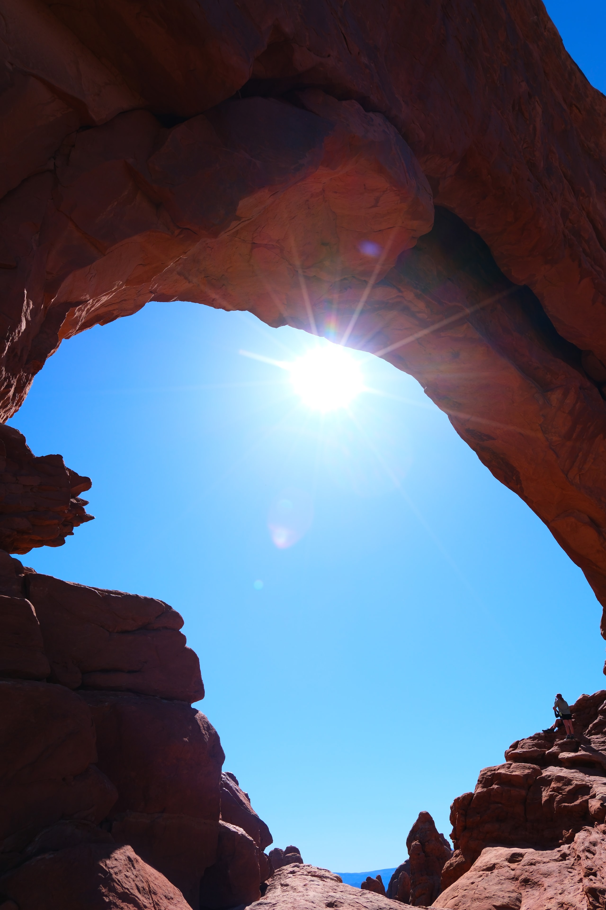 Looking up through North Window heart shaped opening with dramatic sun starburst and warm orange red sandstone at Arches National Park Utah