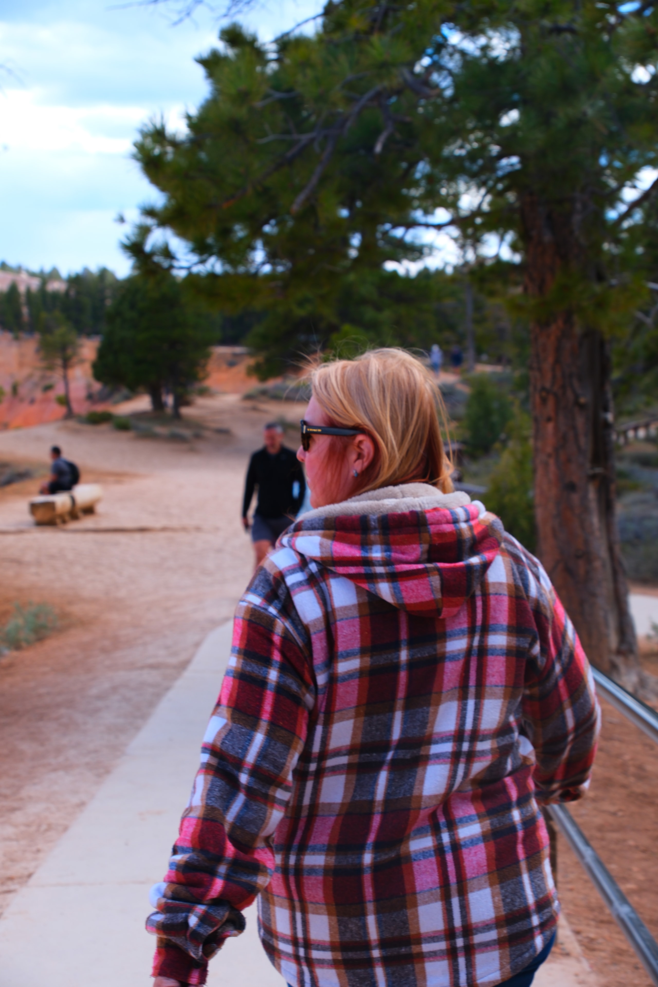 Tina on trail with orange red canyon walls behind ponderosa pine and other visitors at Bryce Canyon National Park Utah