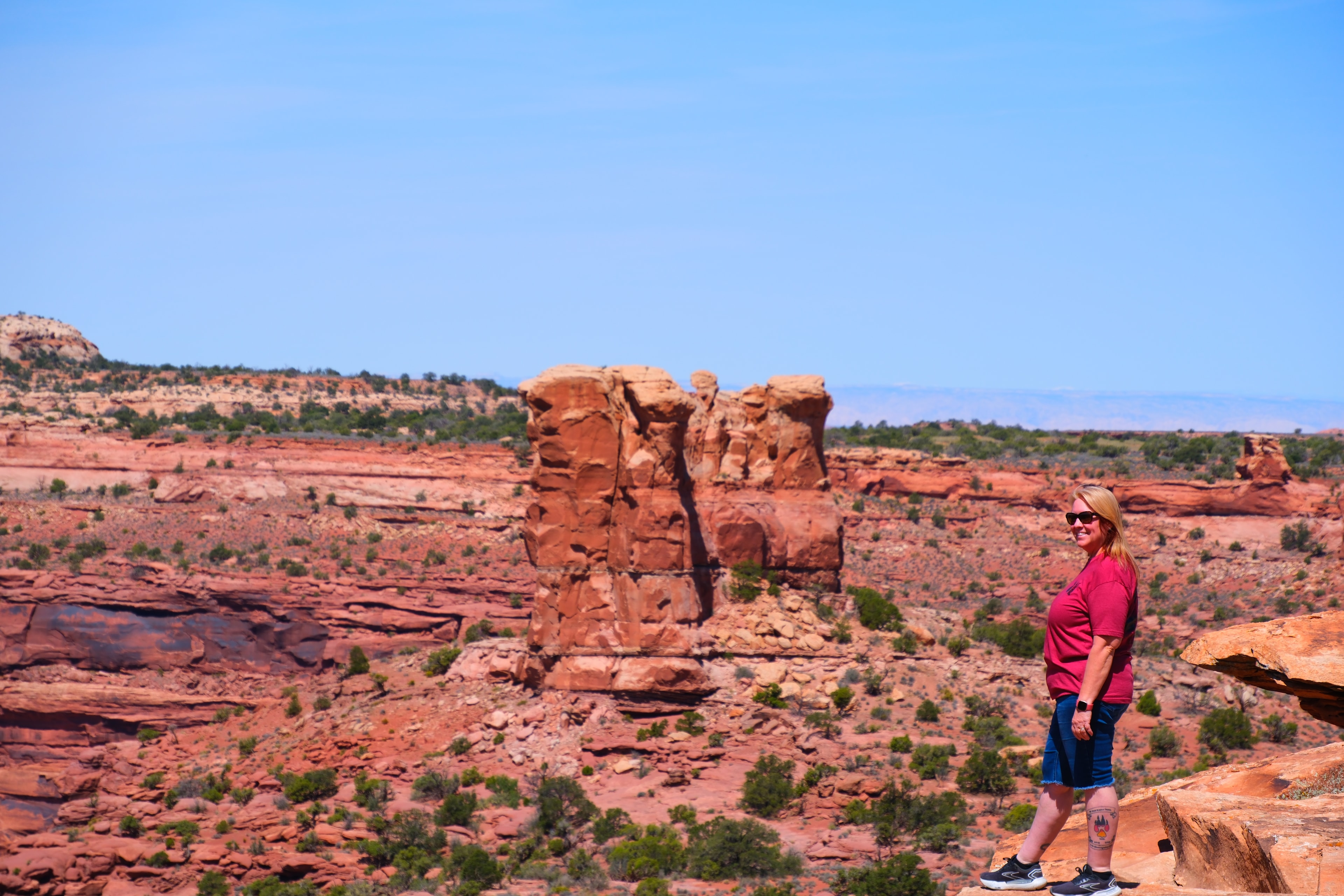 Tina standing on slickrock with cluster of red sandstone formations behind and junipers and blue sky at Canyonlands National Park Utah