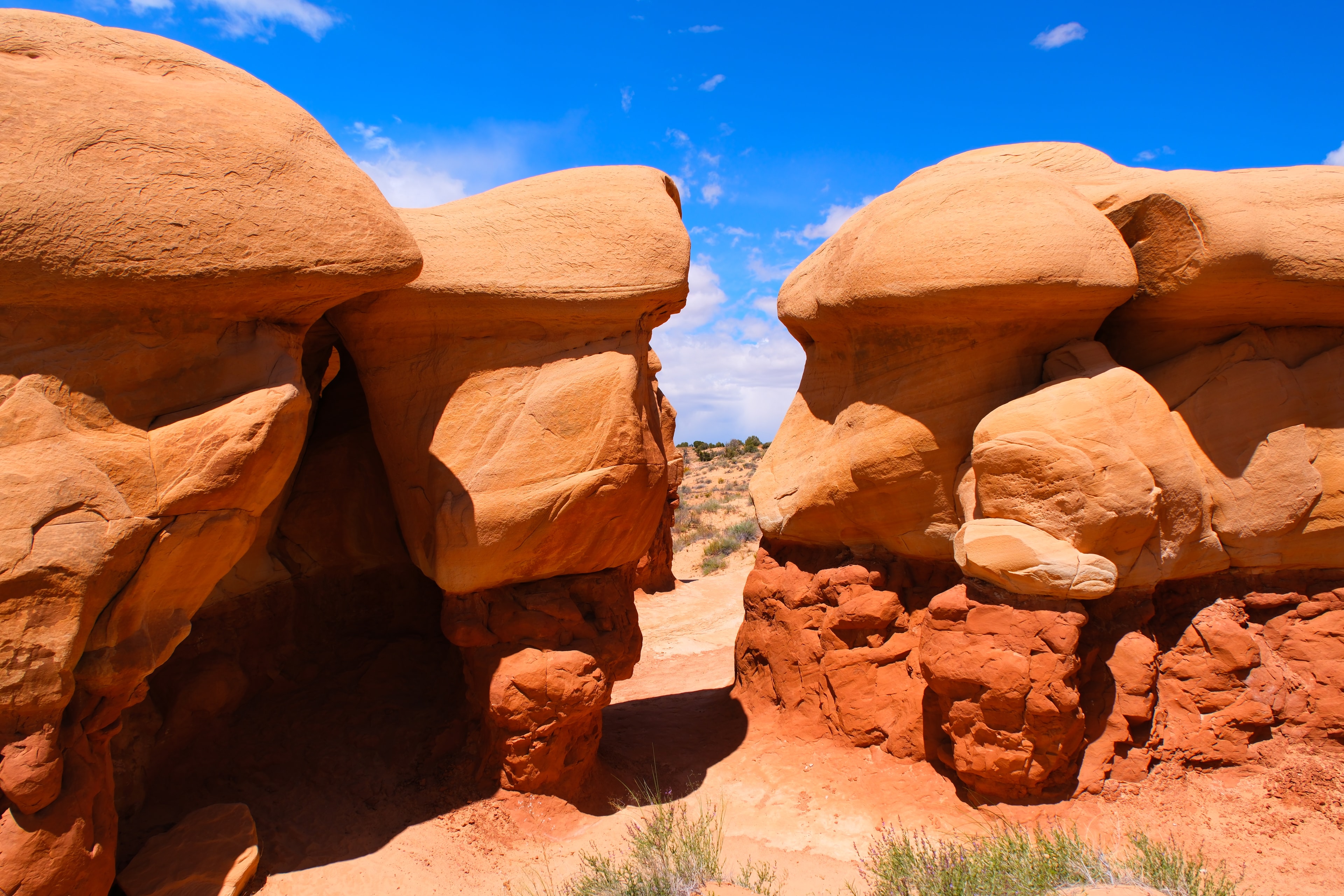 Two facing orange sandstone mushroom cap hoodoos with a gap passage between them and blue sky at Devil's Garden Utah