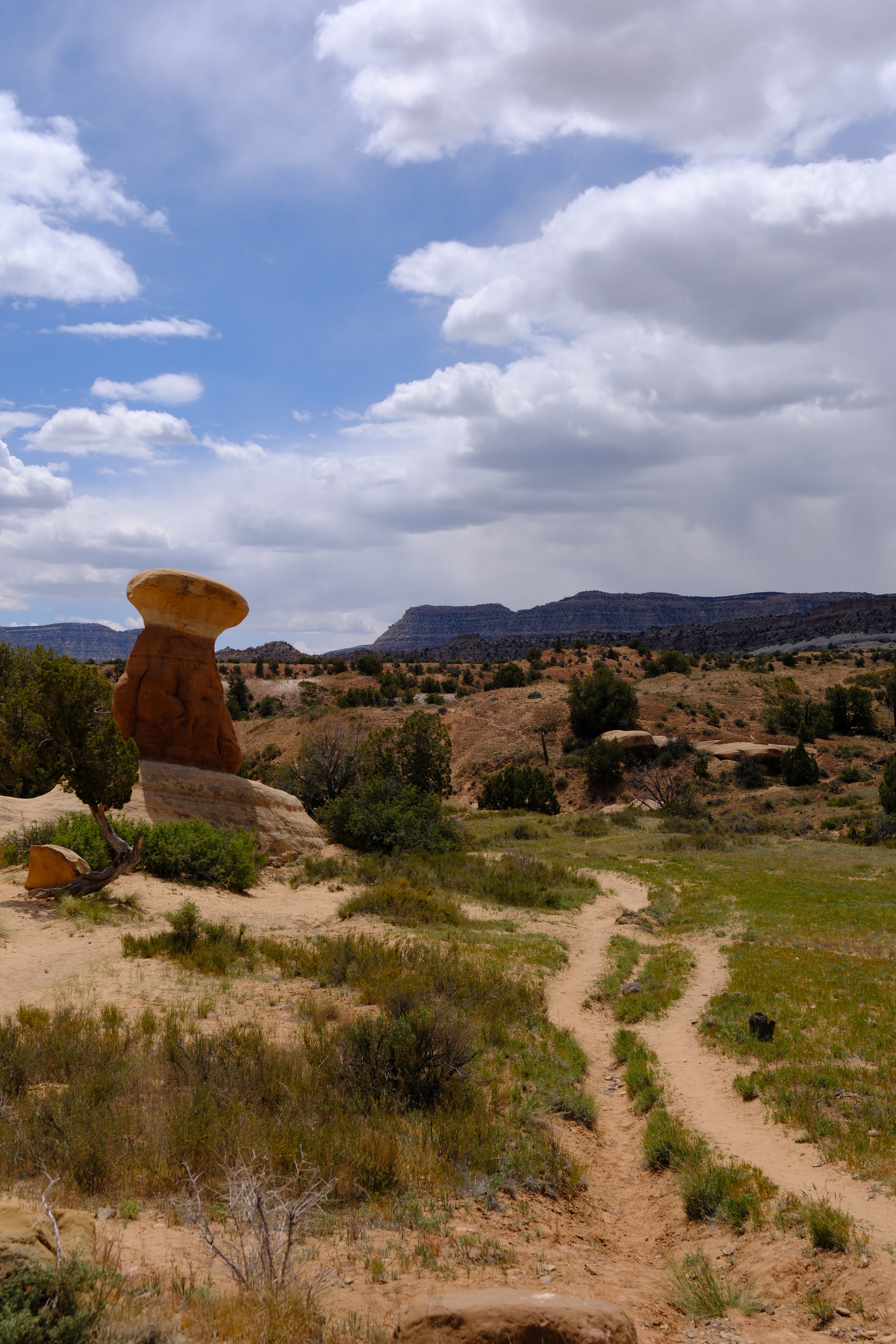 Lone orange sandstone mushroom cap hoodoo with wide desert valley and clouds behind at Devil's Garden Utah