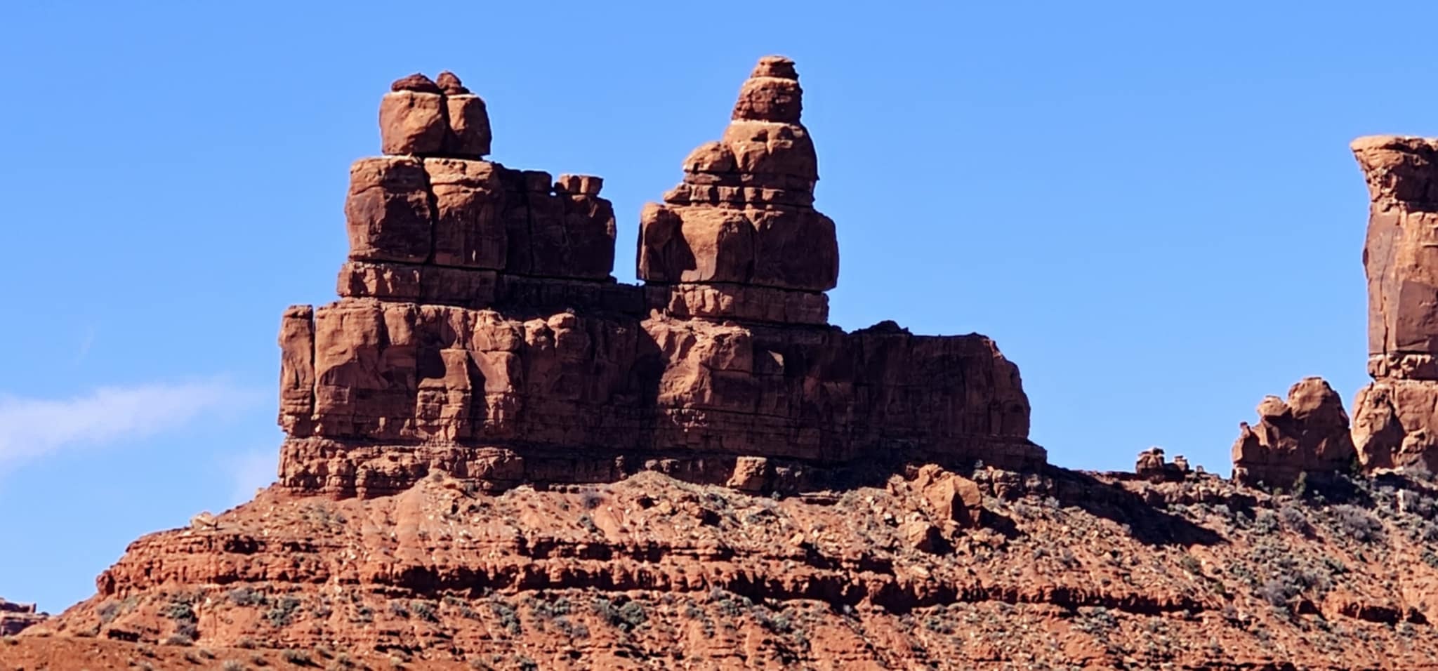 Twin stacked sandstone buttes with layered red rock formations rising against a deep blue sky in Valley of the Gods Utah