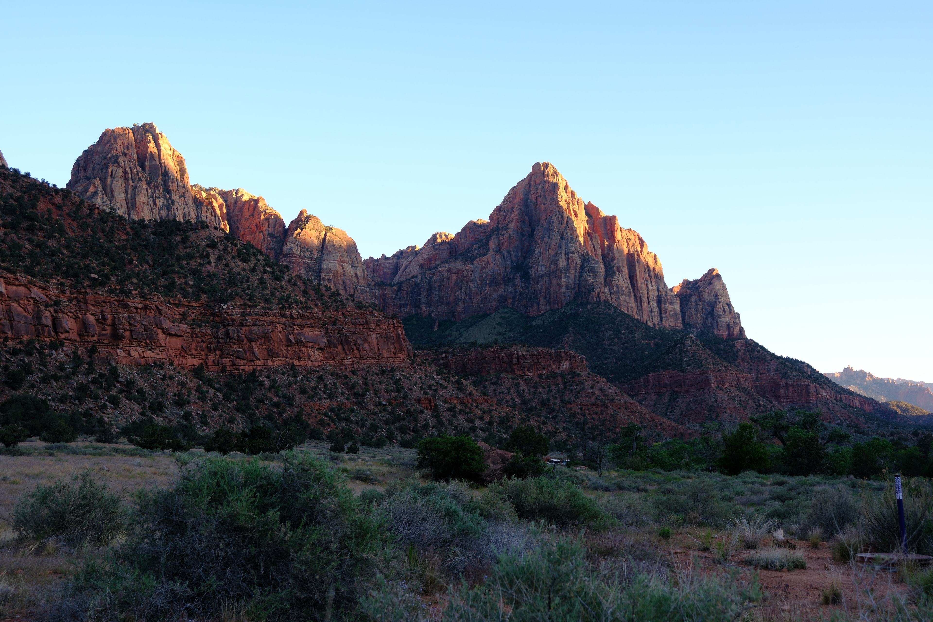 The Watchman at golden hour with warm alpenglow on jagged red and cream peaks sagebrush desert floor clear blue sky at Zion National Park Utah LOVING LIFE HAVING FUN Brinkley Z3400