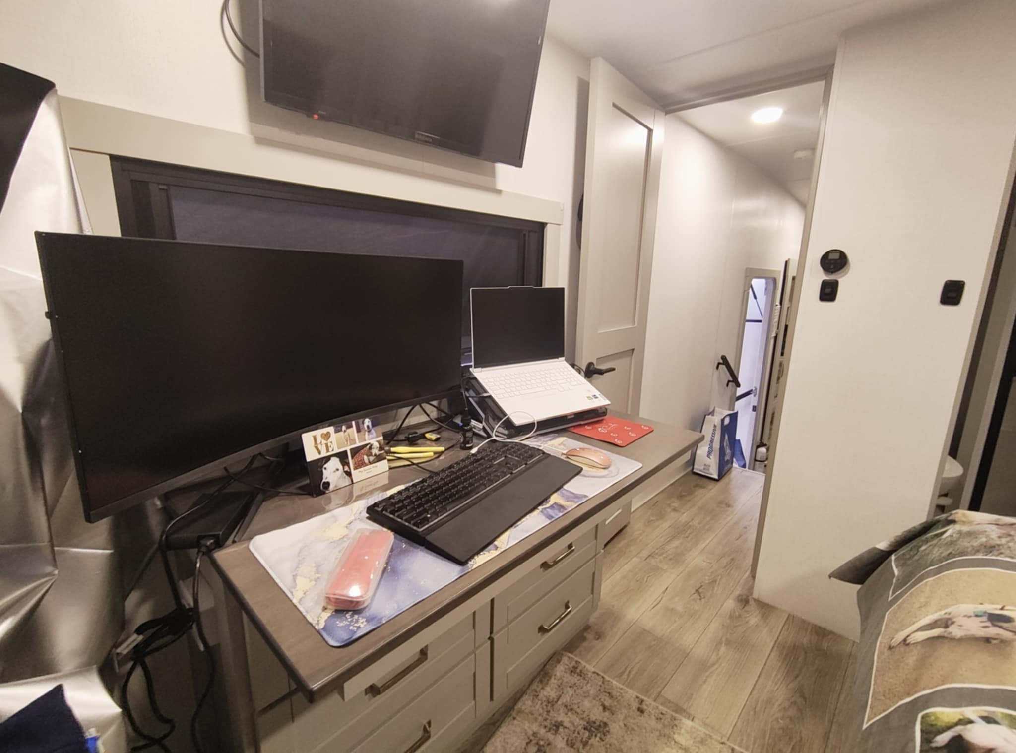 Wide view of Tina's Brinkley Z3400 office at night — curved monitor, laptop, keyboard, and hallway beyond