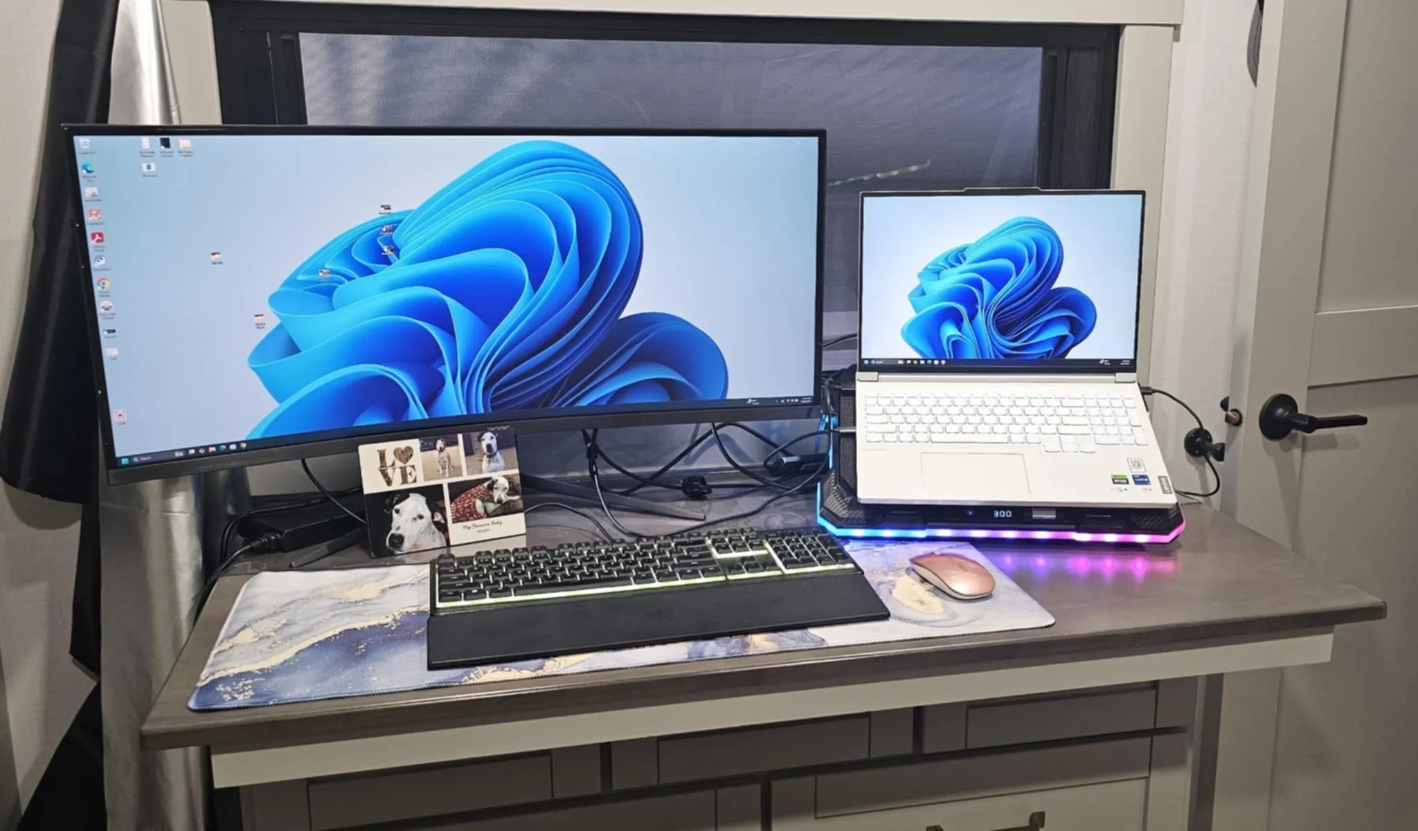Tina's dual-monitor setup in the Brinkley Z3400 — curved monitor, white laptop with RGB stand, marble desk mat, and dog photo frame